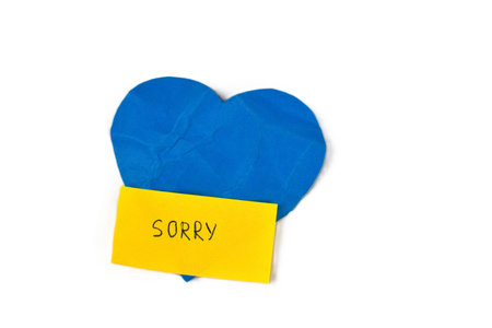 Blue heart shape with yellow paper note saying â€œSorryâ€ isolated on white background....