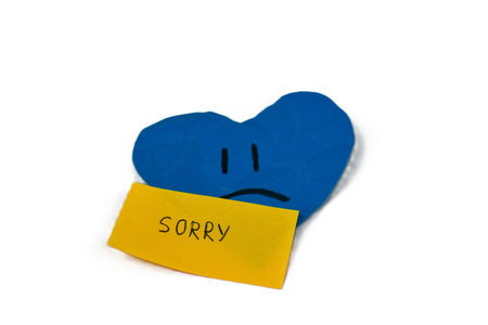Blue heart with sad facial expression and yellow sticky note saying â€œSorryâ€ isolated on...