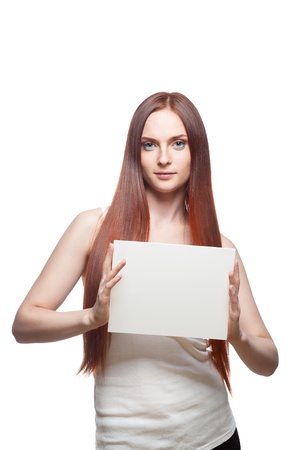 vertical studio portrait of young attractive green-eyed caucasian female with long natural straight red hair which holding white empty cardboard signの写真素材