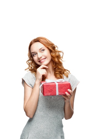 young red-haired casual girl with red gift looking away with thoughtful expression on face の写真素材