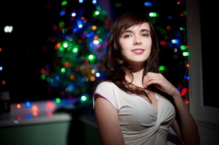 portrait of young smiling brunette caucasian woman over christmas tree and lights on backgroundの写真素材