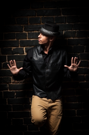 young caucasian man in black shirt and hat lean against black brick wallの写真素材
