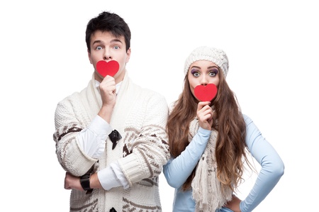 young casual caucasian brunette couple in winter clothing cover their mouths with red hearts and looking at camera with wide opened eyesの写真素材