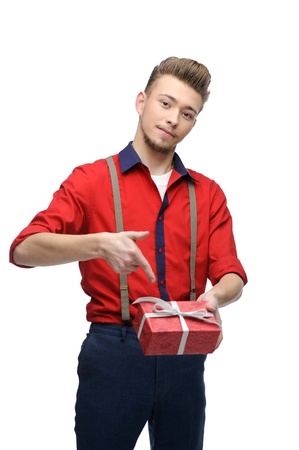 cheerful young caucasian man in red vintage clothing holding and pointing at gift isolated on whiteの写真素材