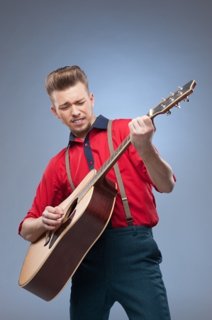 caucasian young vintage man in red shirt playing guitar over blue backgroundの写真素材