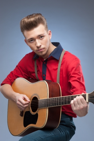 caucasian young vintage man in red shirt playing guitar over blue backgroundの写真素材