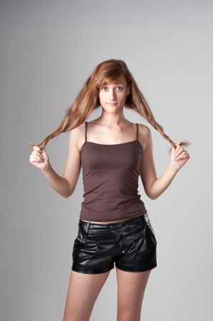 cheerful casual caucasian girl holding her long brown hair on gray backgroundの写真素材