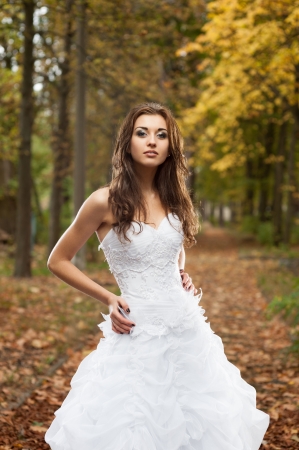 outdoors portrait of beautiful young caucasian brunette woman in white wedding dress over green foliage on backgroundの写真素材