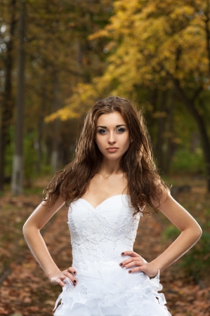 outdoors portrait of beautiful young caucasian brunette woman in white wedding dress over green foliage on backgroundの写真素材