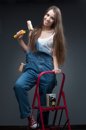happy smiling painter woman standing at ladder and holding rollの写真素材