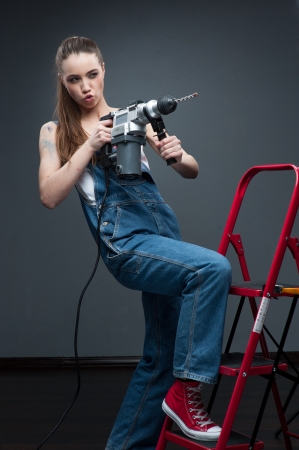 young funny woman standing at ladder and holding puncherの写真素材