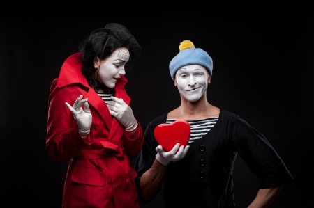 two funny mimes holding red heart isolated on black backgroundの写真素材