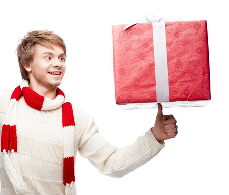 portrait of young cheerful smiling caucasian man which balancing  red christmas gift on thumb with happy smileの写真素材