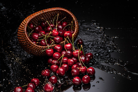 fresh red cherry falling from brown basket over water waveの写真素材