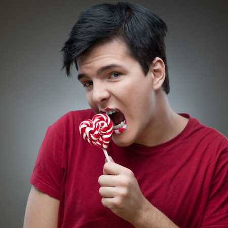 young funny caucasian brunette man in red t-shirt holding lollipop with open mouthの写真素材