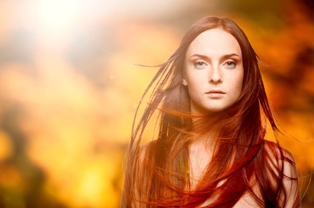 beautiful young woman with windy red hair over autumn backgroundの写真素材