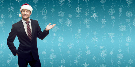 smiling young business man in santa hat showing empty space over winter snowflakes backgroundの写真素材