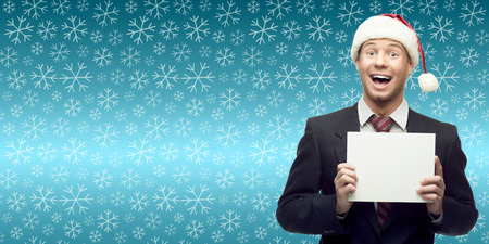smiling young business man in santa hat holding sign over winter snowflakes backgroundの写真素材