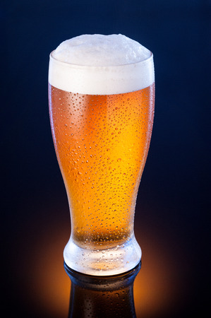light cold beer in frosty glass over dark blue backgroundの写真素材
