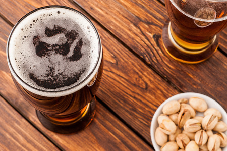 galss of dark cold frothy beer, nuts on an old wooden table