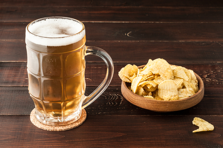 glass of cold frothy lager beer and potato chips plate on an old wooden tableの写真素材