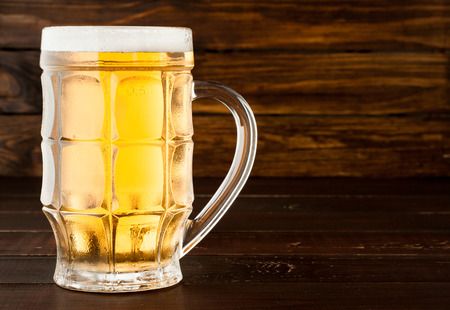 glass of cold frothy lager beer on an old wooden tableの写真素材