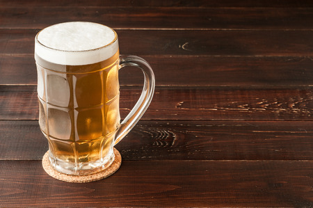 glass of cold frothy lager beer and potato chips plate on an old wooden tableの写真素材