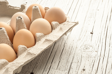 chicken eggs in cardboard box over white wooden backgroundの写真素材