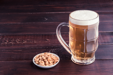 glass of cold frothy lager beer and peanuts plate on an old wooden tableの写真素材