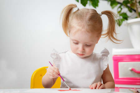 Cute adorable baby girl learning painting with water colors. Little toddler child drawing at home, using colorful brushes. Healthy happy daughter experimenting with colors, water at home or nursery.の写真素材