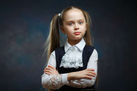 Serious Calm Girl Ponytail Hairstyle Portrait. Closeup Schoolgirl Front Camera Shot. Smart Preschool Child Fold Arm on Chest. Pensive Female Pupil Wear Black and White Uniformの写真素材