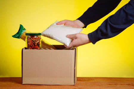 A volunteer puts food in a donation box. Assistance to the poor people under conditions of self-isolation during a pandemic coronavirus.の写真素材