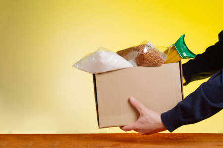 Volunteer with donation box with foodstuffs on yellow backgroundの写真素材