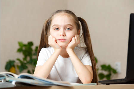 Distance or remote learning. Pupil want to sleep. Tired schoolgirl with hand on face sitting at laptop. Online school. Coronavirus Pandemic Conceptの写真素材