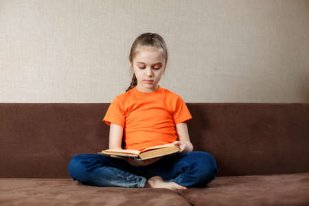 Adorable little girl reading a book in her homeの写真素材