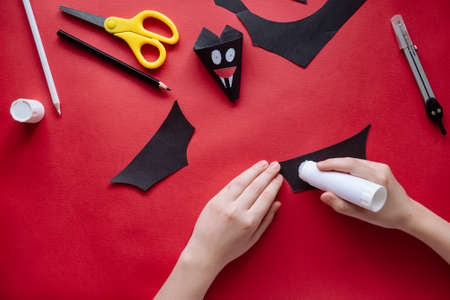 How to make bat out of paper at home. Hands making craft out of paper. Step by step photo instruction. Step 10. Glue the wings. Children DIY art projectの写真素材
