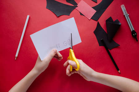 How to make bat out of paper at home. Hands making craft out of paper. Step by step photo instruction. Step 8. Cut out the eyes and fangs. Children DIY art projectの写真素材
