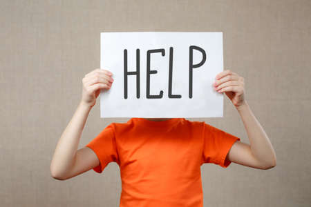 Little girl holding a piece of paper with the word Help in front of herの写真素材