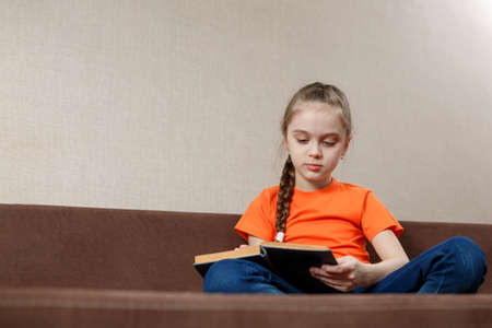 Portrait of nice attractive lovely focused cheerful teen girl wearing orange t-shirt sitting in...