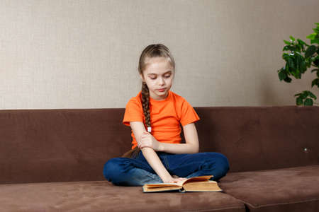 Portrait of nice attractive lovely focused cheerful teen girl wearing orange t-shirt sitting in lotus pose in sofa at home.の写真素材