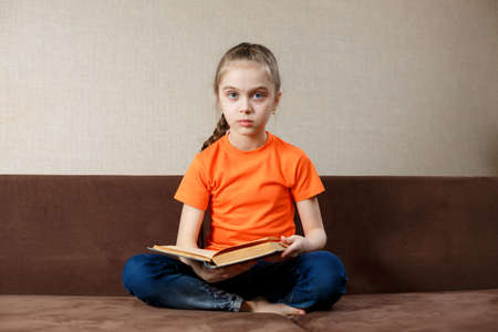 Little girl with book on her legs looking at camera.の写真素材