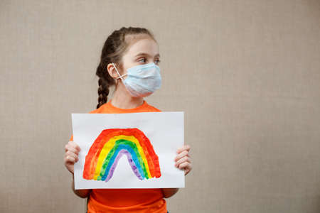 A child shows a drawing of a rainbow during pandemic coronavirus quarantine. Stay at home Social media campaign for coronavirus prevention, let's all be well, hope during coronavirus pandemic concept.の写真素材