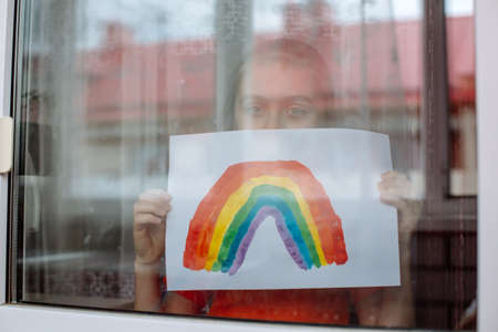 Little Girl painting rainbow during Covid-19 quarantine at home. Kid near window. Stay at home Social media campaign for coronavirus prevention.の写真素材