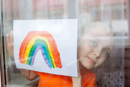 Little Girl painting rainbow during Covid-19 quarantine at home. Kid near window. Stay at home Social media campaign for coronavirus prevention.の写真素材