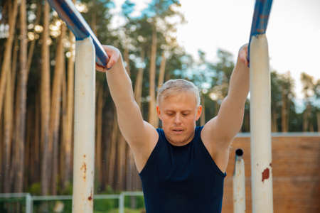 fitness, sport, exercising, training and lifestyle concept - young man doing triceps dip on parallel bars outdoorsの写真素材