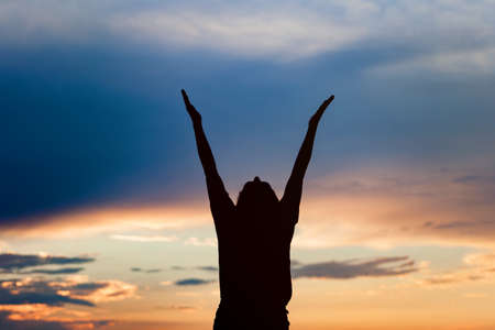 Happy celebrating winning success woman at sunset or sunrise standing elated with arms raised up...