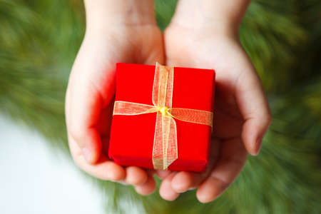 holidays, present, childhood and happiness concept - close up of child hands with gift box over christmas tree backgroundの写真素材