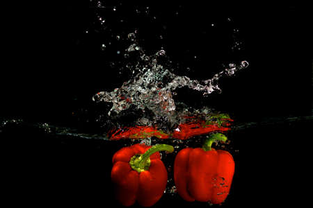 Red pepper in water with splashes on black backgroundの写真素材