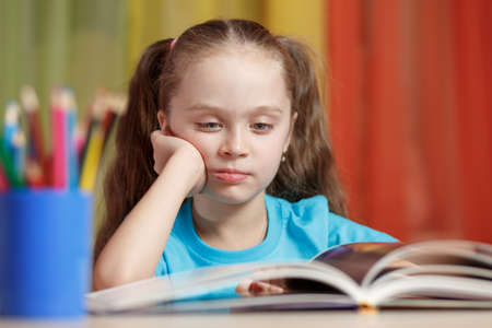 Pensive little girl touching her cheek and thinking about something and read a bookの写真素材