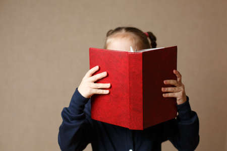 Beautiful baby covering her face with a book. Back to school.